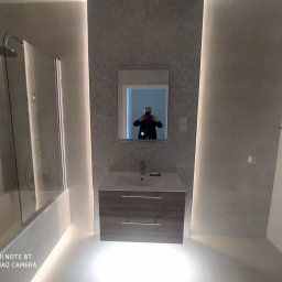 KAROL-BUD Mirosław Bloch - Nowoczesna łazienka z podświetleniem LED, kabiną prysznicową, umywalką z szafką w odcieniach drewna i lustrem, w którym odbija się osoba robiąca zdjęcie.