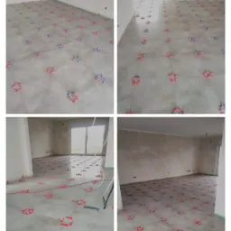 Układanie szarych płytek podłogowych z użyciem systemu poziomowania z czerwonymi i niebieskimi klinami w przestronnym, surowym wnętrzu.