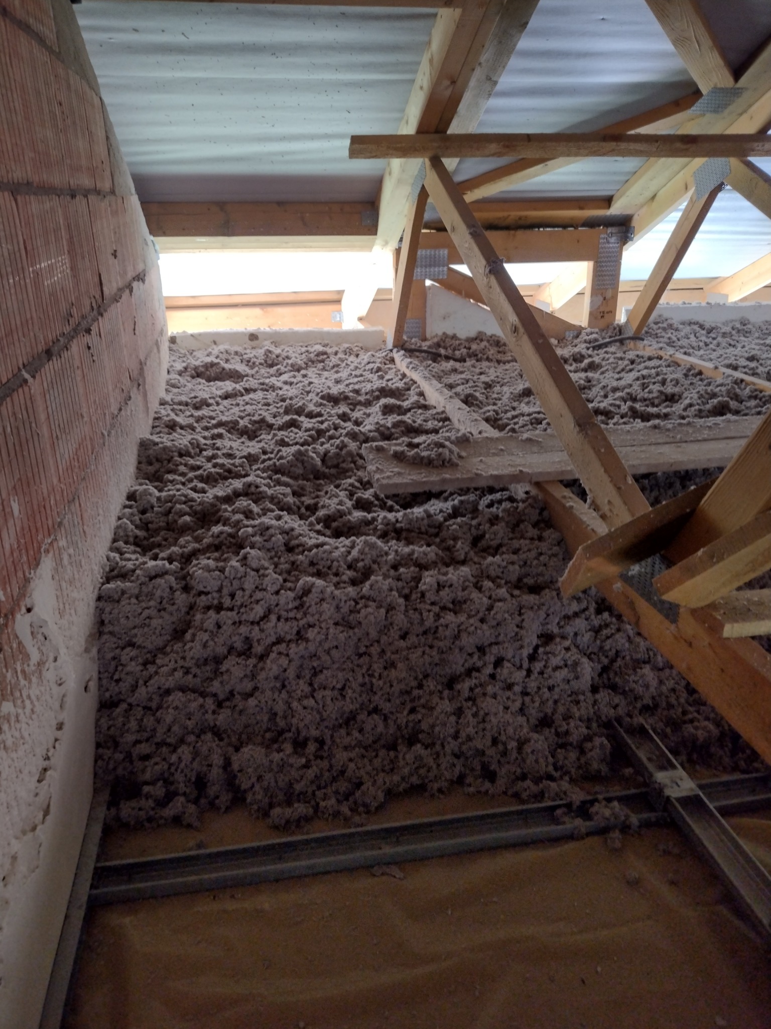 Poddasze z widoczną warstwą izolacji z wełny mineralnej, drewniana konstrukcja więźby dachowej, fragment muru z cegły.