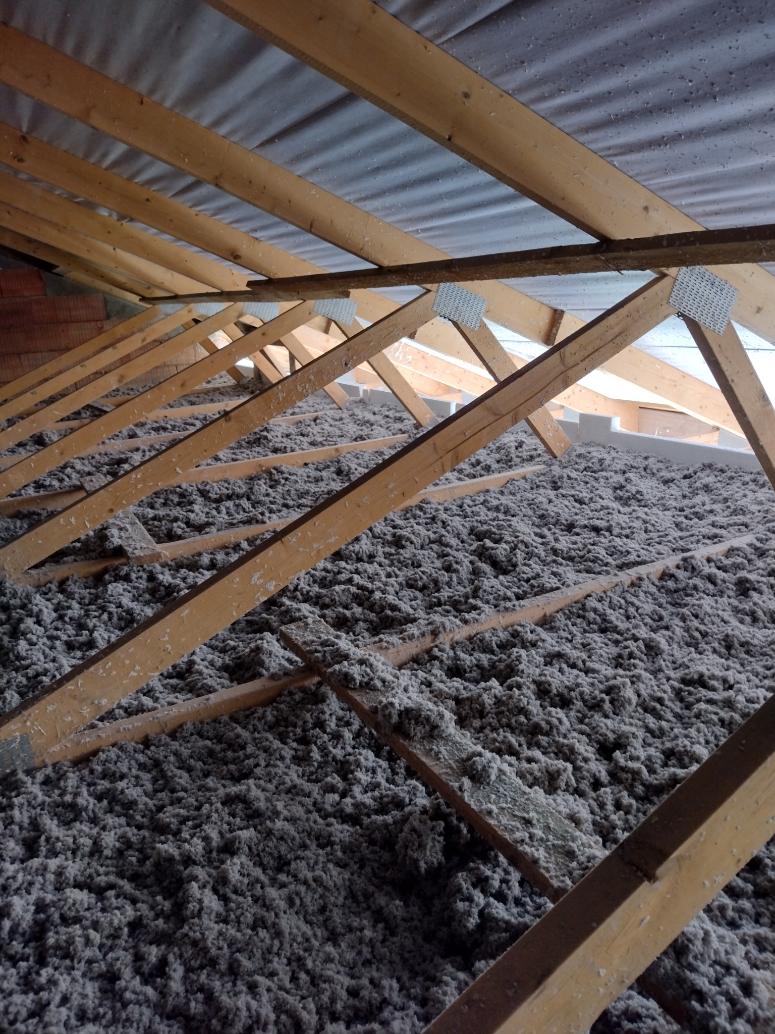 Poddasze z drewnianą konstrukcją i szarą wełną mineralną jako izolacja termiczna, widok z góry.