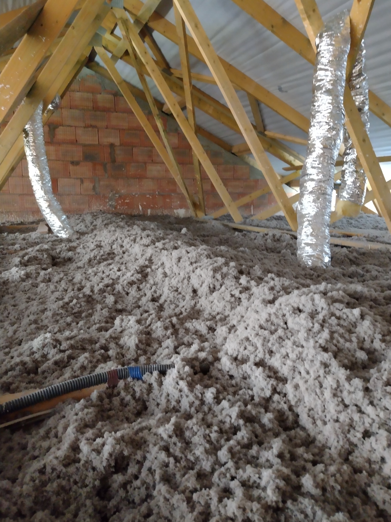 Poddasze w Dmosinie wypełnione szarą wełną izolacyjną, widoczne drewniane krokwie i aluminiowe rury wentylacyjne.