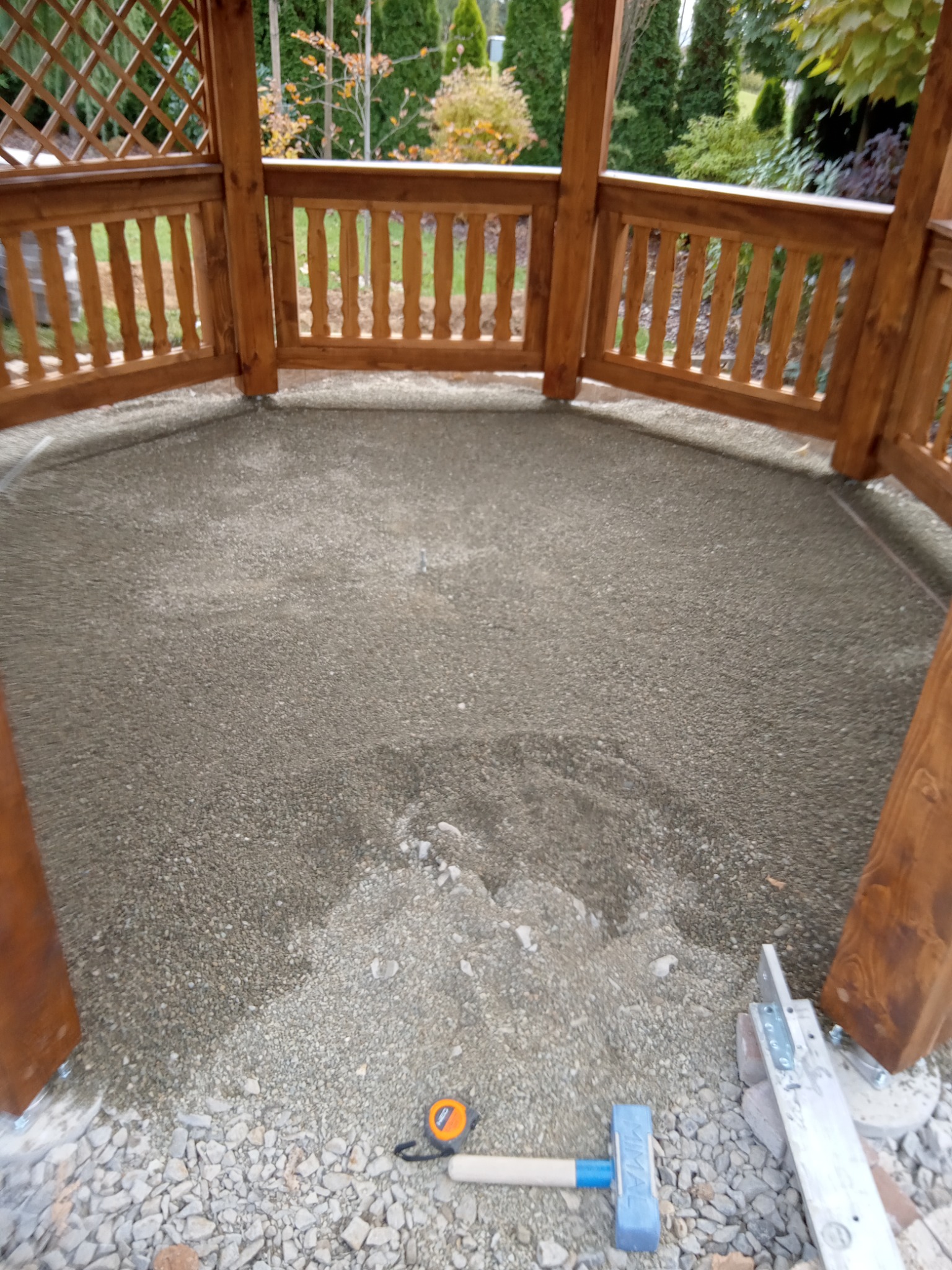 Przygotowanie podłoża pod wylewkę w drewnianej altanie ogrodowej, widoczne narzędzia: młotek gumowy, miarka i poziomica.