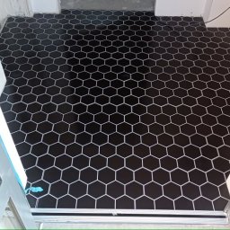 Łukasz Przespolewski - Ułożona czarna, heksagonalna podłoga z białymi fugami, widok z progu drzwi, z widocznymi rurami przy ścianie.