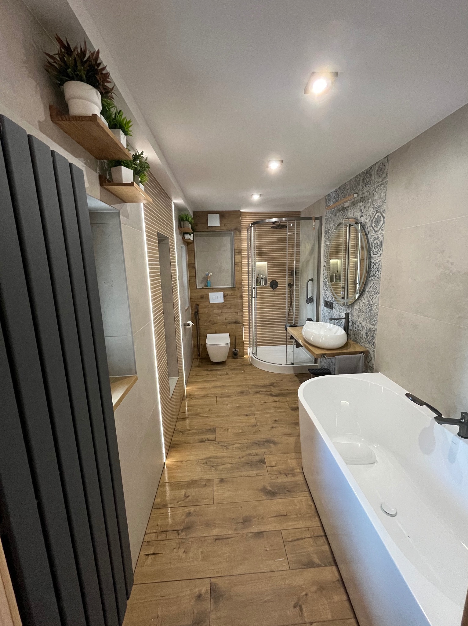 Nowoczesna łazienka z drewnianą podłogą, kabiną prysznicową, wanną i umywalką na drewnianym blacie. Dekoracyjne płytki i oświetlenie LED dodają elegancji.