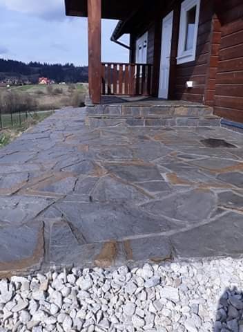 Kamienny chodnik z nieregularnych płyt prowadzący do drewnianego domu z widokiem na krajobraz