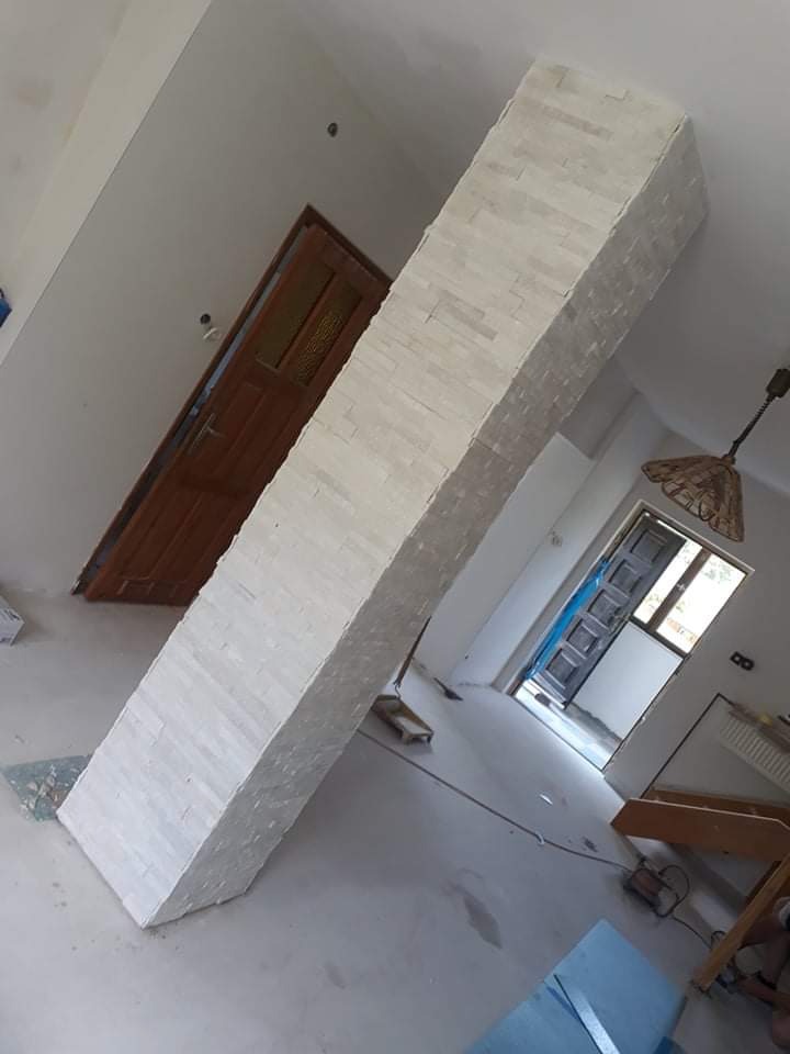 Wykończony filar w salonie, obłożony dekoracyjną, jasną okładziną imitującą kamień, widoczna stara stolarka drzwiowa w tle.