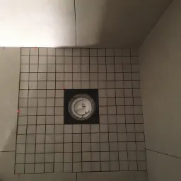 Podłoga łazienki w trakcie układania mozaiki z odpływem liniowym, widoczne poziomica i buty, czerwone krzyżyki dystansowe