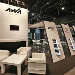 Stoisko targowe z logo AWA, WIDIA i Lamina Technologies, wyposażone w białe meble i ekspozytory z oświetleniem LED, prezentujące minimalistyczny design.