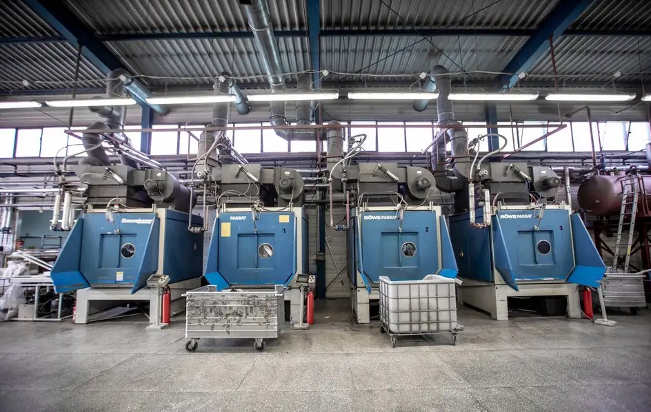 Cztery przemysłowe maszyny do czyszczenia dywanów w hali w Żywcu, z widocznymi metalowymi wózkami i rurami wentylacyjnymi pod sufitem.