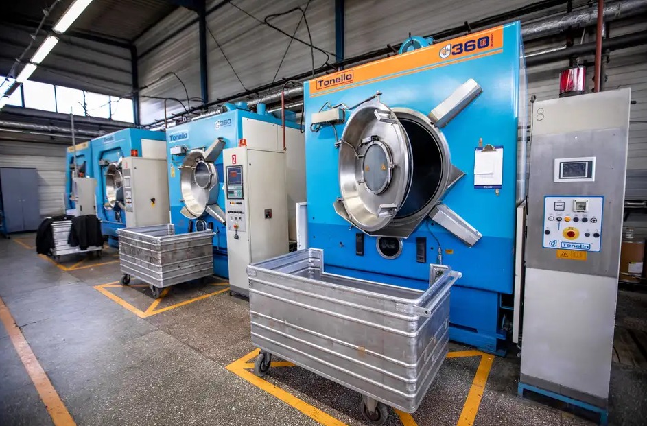 Przemysłowe pralnico-wirówki Tonello 360 z otwartymi drzwiami bębna i wózkami na pranie w pomieszczeniu pralni.
