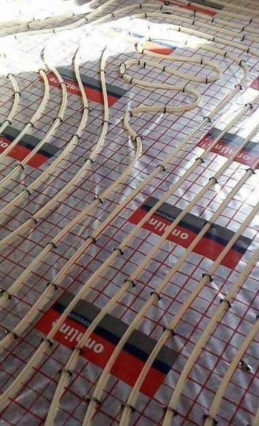 Rozłożone rury ogrzewania podłogowego na folii z siatką, widoczne uchwyty mocujące rury.