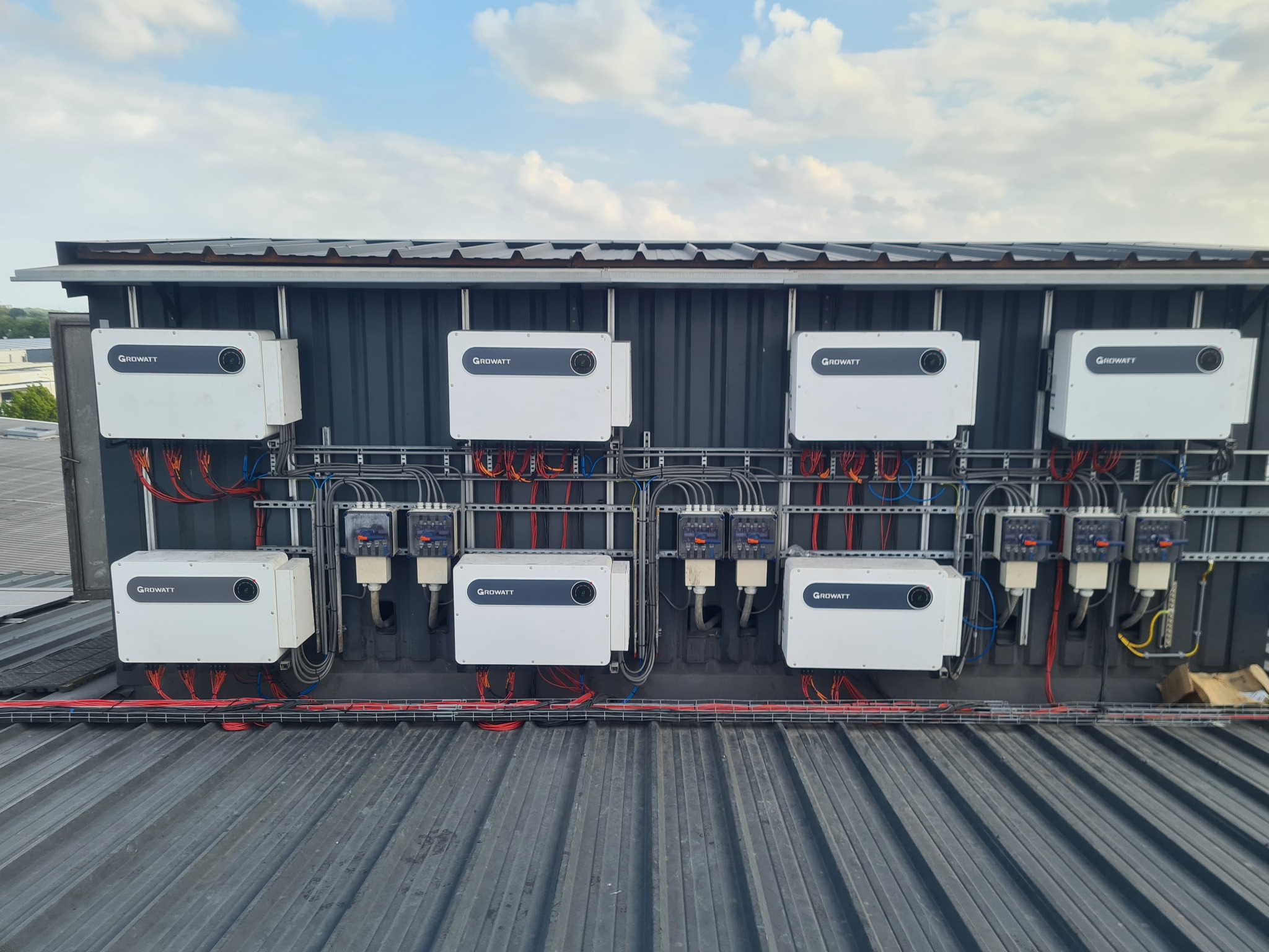 Rząd paneli fotowoltaicznych marki Growatt zamontowanych na metalowej konstrukcji, widoczne przewody i zabezpieczenia elektryczne.