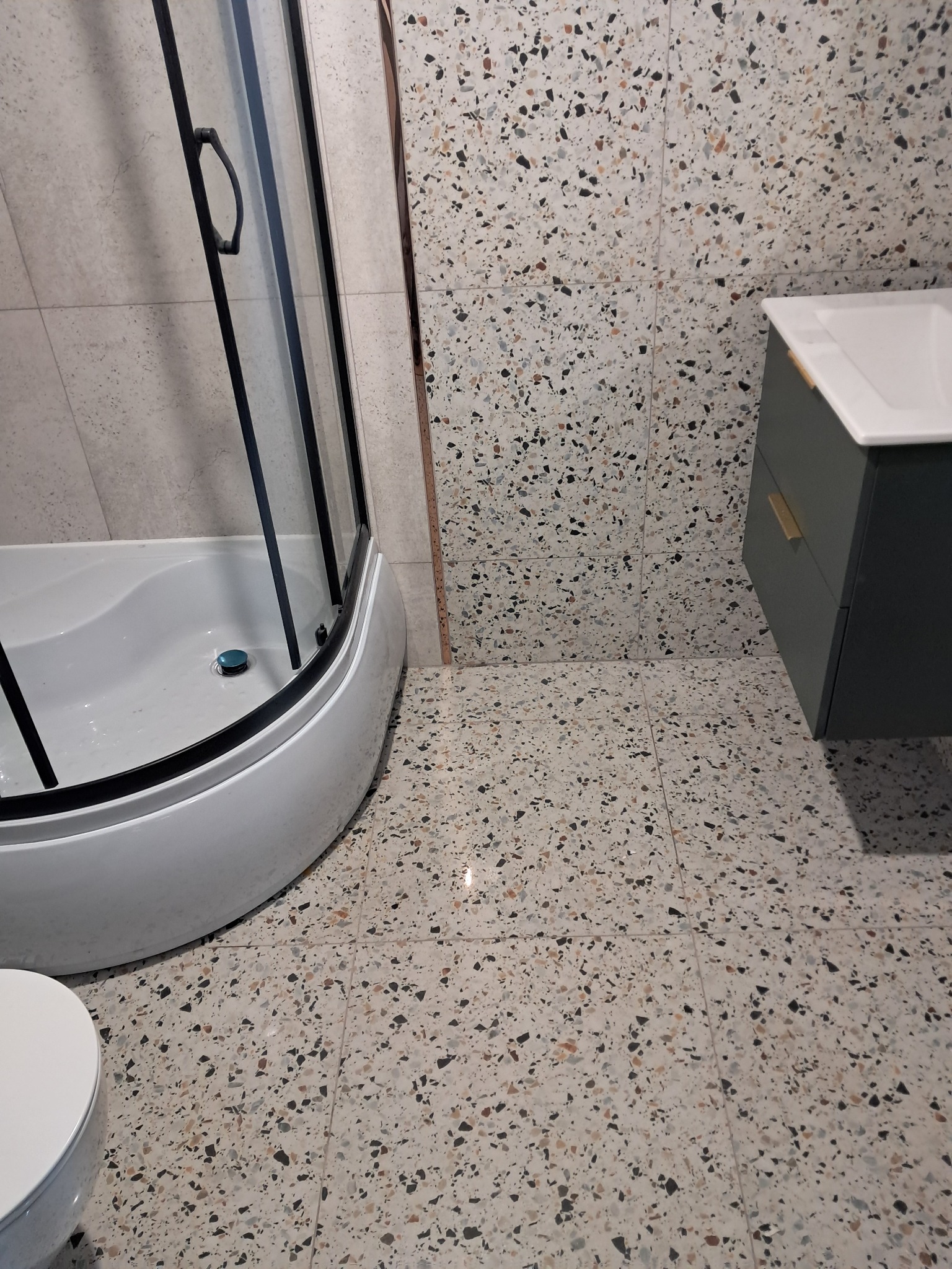 Nowoczesna łazienka z kabiną prysznicową, umywalką i toaletą. Dominuje wzór lastryko na ścianach i podłodze. Użyto czarnych i białych elementów.