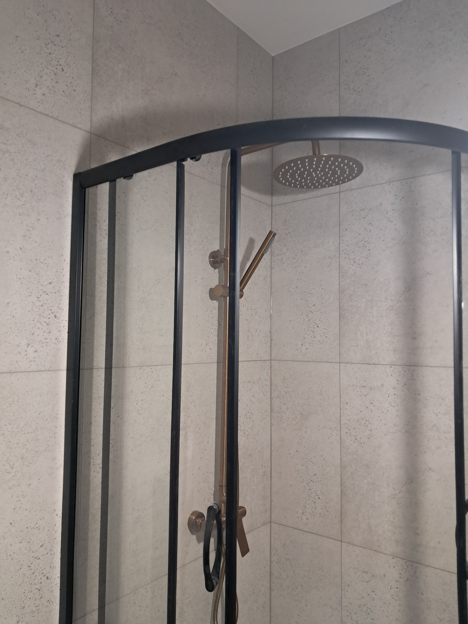 Nowoczesna kabina prysznicowa z czarnymi ramami i deszczownicą w łazience wykończonej jasnymi płytkami. Widok z bliska na detale wykończenia.