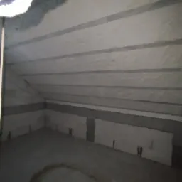 Poddasze z ukończoną izolacją pianką PUR, widoczne szare belki konstrukcyjne i nier&oacute;wnomierna powierzchnia piany.