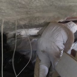 CLEAN-PUR Paweł Mateusiak - Pracownik w kombinezonie ochronnym aplikuje piankę izolacyjną na stropie, widoczne przewody i folia ochronna.