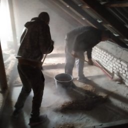 CLEAN-PUR Paweł Mateusiak - Dwóch pracowników w trakcie sprzątania poddasza po wykonaniu izolacji, widoczne resztki materiału izolacyjnego i wiadro.