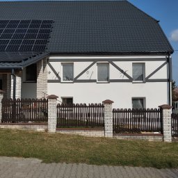 CLEAN-PUR Paweł Mateusiak - Dom jednorodzinny z panelami słonecznymi na dachu i elewacją w stylu muru pruskiego, okna zabezpieczone folią malarską, ogrodzenie drewniano-murowane.