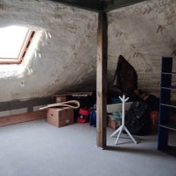 CLEAN-PUR Paweł Mateusiak - Poddasze po nałożeniu izolacji pianką poliuretanową, widoczne okno dachowe, drewniany słup oraz kartony i przedmioty leżące na podłodze.