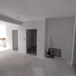 CLEAN-PUR Paweł Mateusiak - Wnętrze w trakcie malowania, widoczne ściany pomalowane na szaro, instalacja grzewcza pod ścianą, oraz otwory drzwiowe bez drzwi.