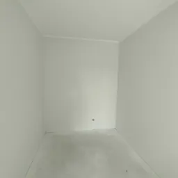 Pusty, świeżo pomalowany pokój z szarymi ścianami i betonową podłogą, widoczne gniazdko elektryczne i listwa przypodłogowa, surowy stan wykończenia.