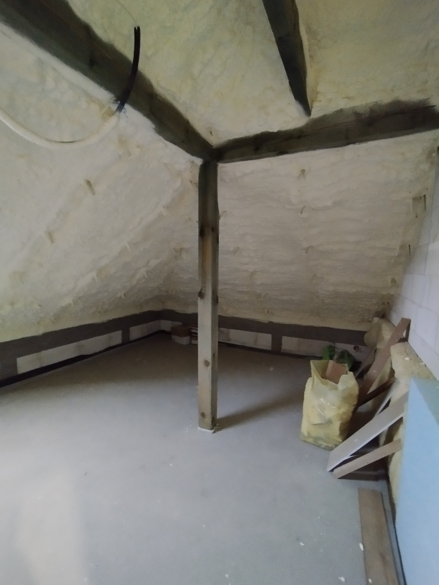 Poddasze po natrysku pianki izolacyjnej, widoczne drewniane belki i elementy konstrukcyjne, na podłodze resztki materiałów budowlanych.