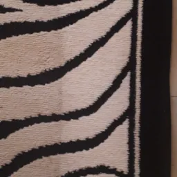 Fragment kremowego dywanu z czarnym, abstrakcyjnym wzorem przypominającym pasy zebry, obramowanego szeroką, czarną bordiurą.