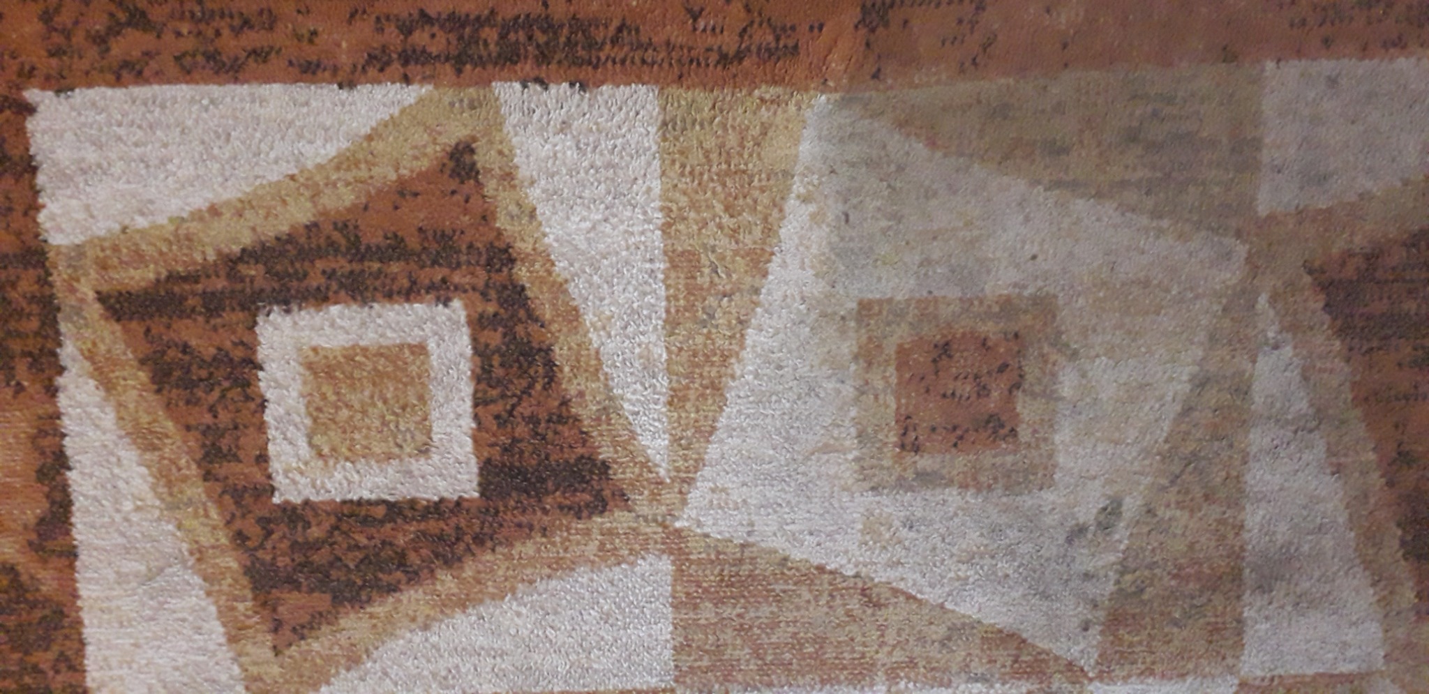 Zbliżenie na wzór geometryczny brązowo-białego dywanu z kwadratami i trójkątami, widoczne włókna materiału.