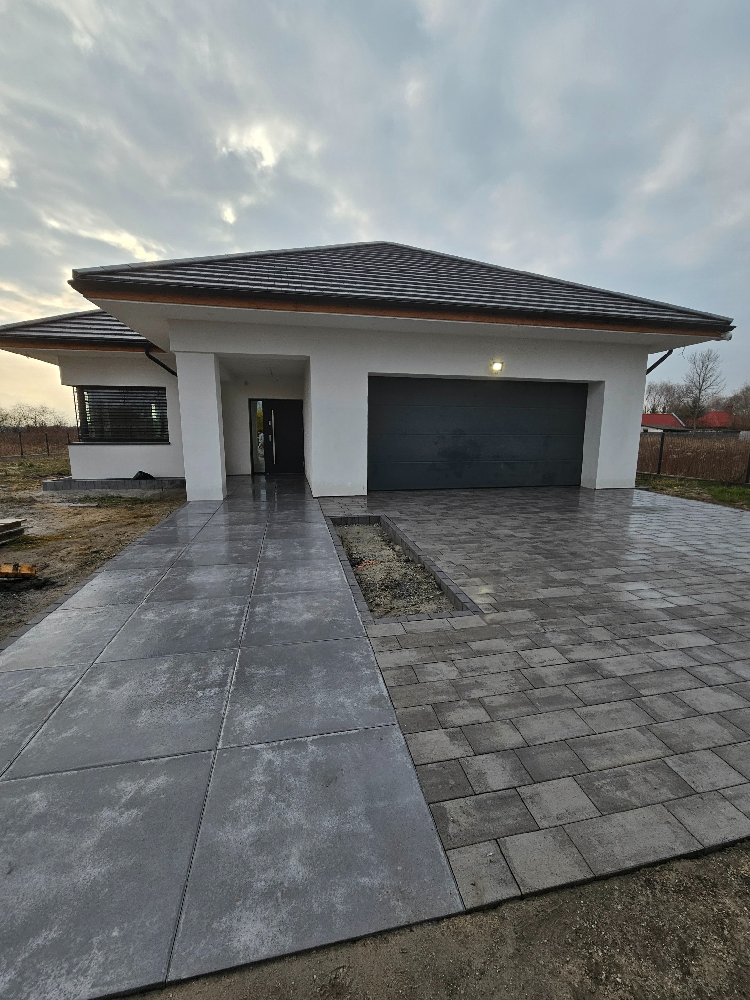 Nowoczesny podjazd z kostki brukowej w dwóch wzorach, prowadzący do domu we Wrocławiu. Duże płyty i mniejsze kostki tworzą estetyczną całość.