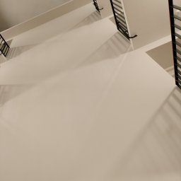 Moki Bud - Widok z góry na klatkę schodową z białymi ścianami i czarnymi metalowymi balustradami, oświetloną ciepłym światłem.