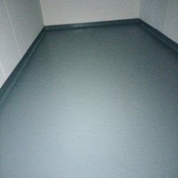 Moki Bud - Szary, świeżo pomalowany narożnik pomieszczenia z widocznymi listwami przypodłogowymi w kolorze ciemniejszego szarego; ściany jasnoszare.