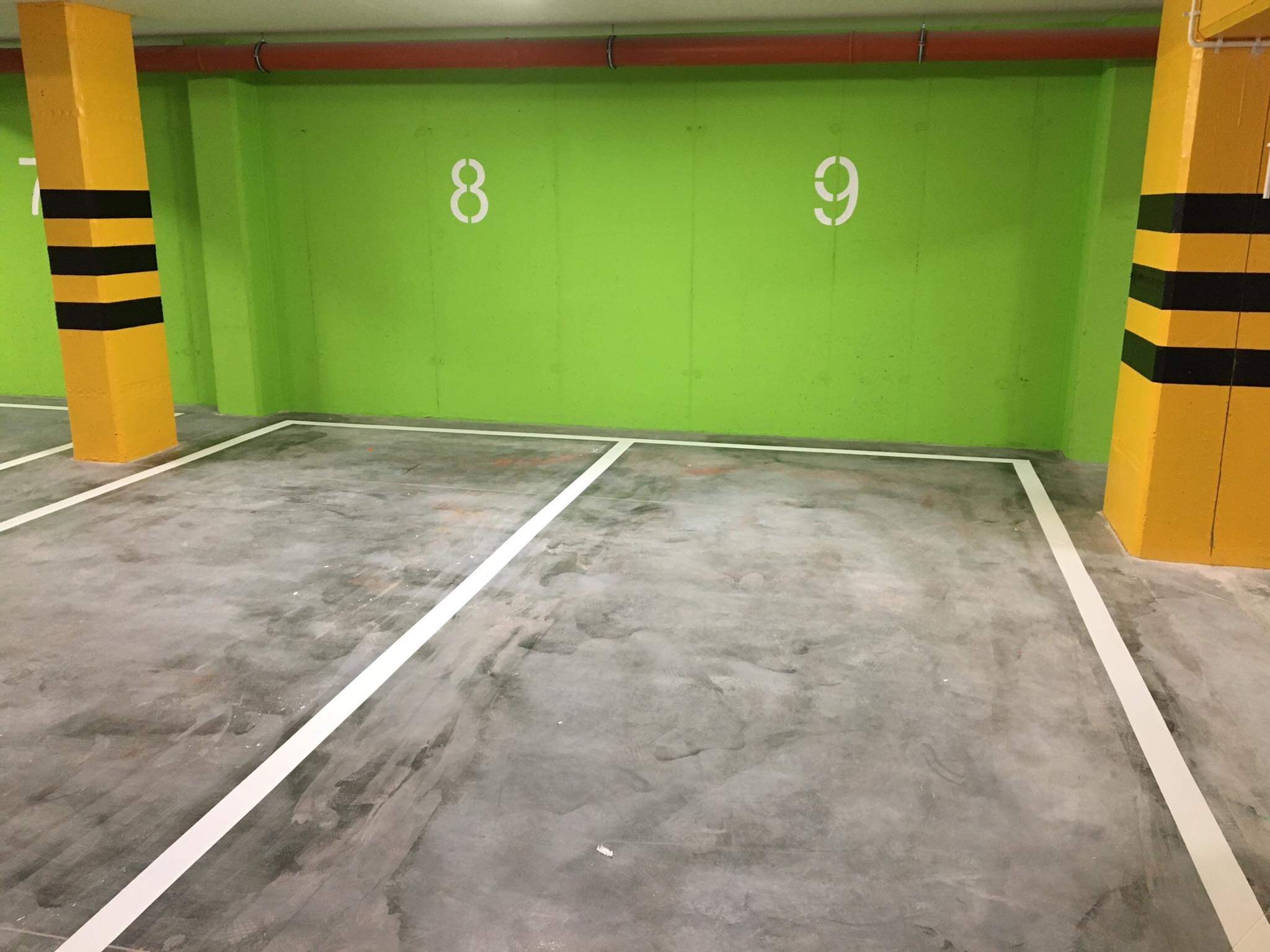 Oznakowane, puste miejsce parkingowe w garażu podziemnym z zielonymi ścianami i żółto-czarnymi słupami.