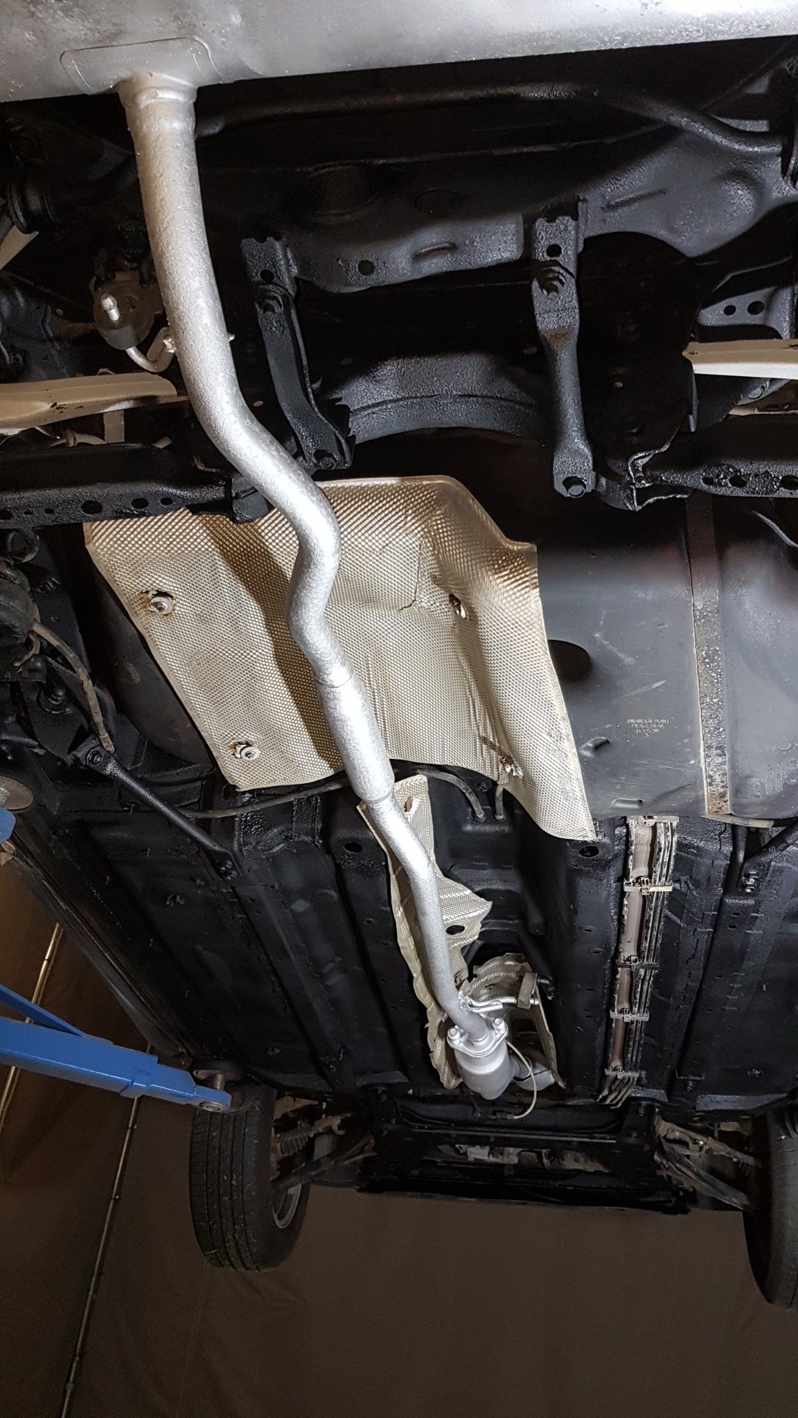 Podwozie samochodu po zabezpieczeniu antykorozyjnym, widoczny srebrny układ wydechowy i osłona termiczna, całość na podnośniku warsztatowym.