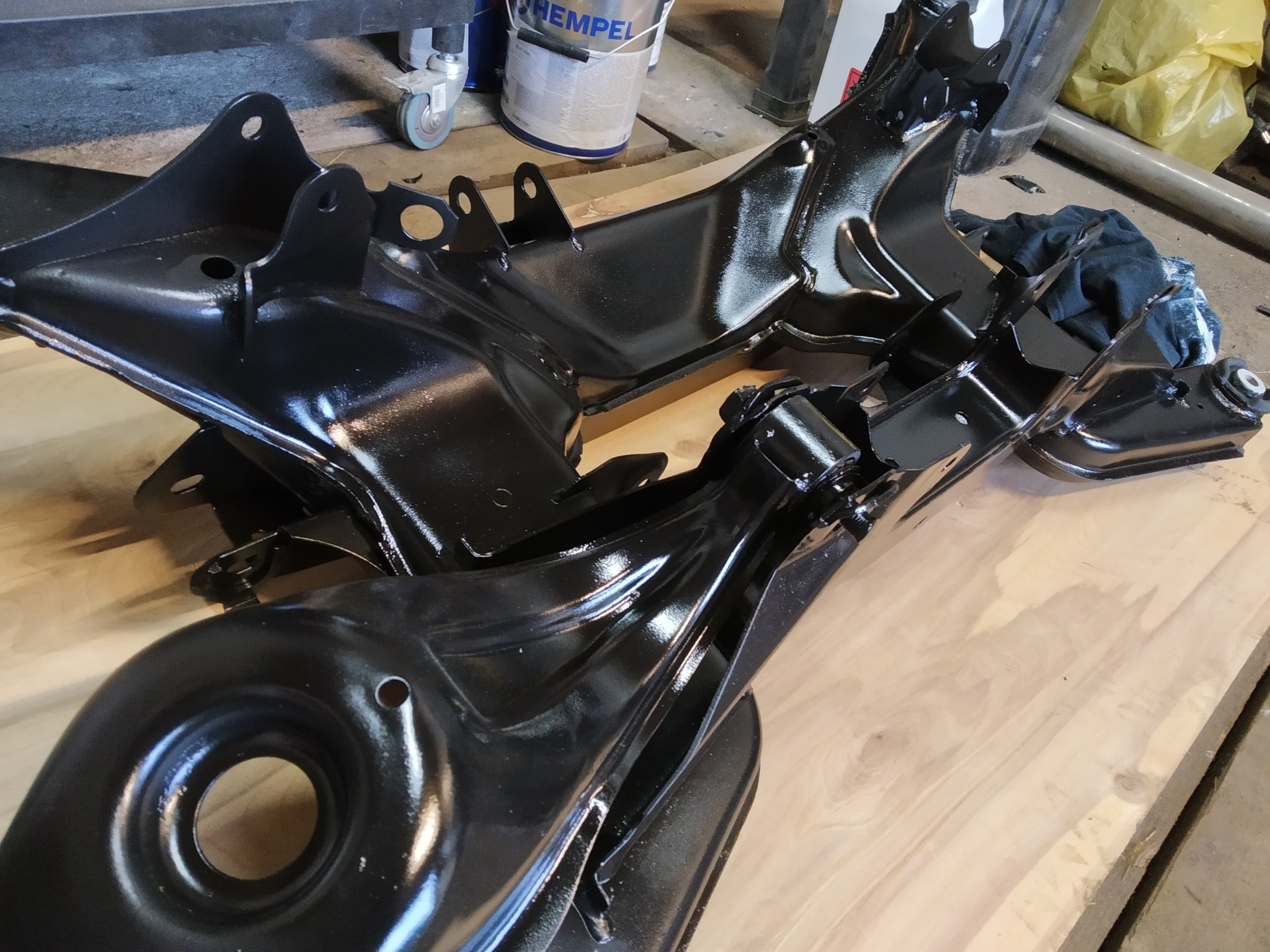 Części samochodowe, prawdopodobnie elementy zawieszenia, po nałożeniu błyszczącej, czarnej powłoki ochronnej na drewnianym blacie roboczym.