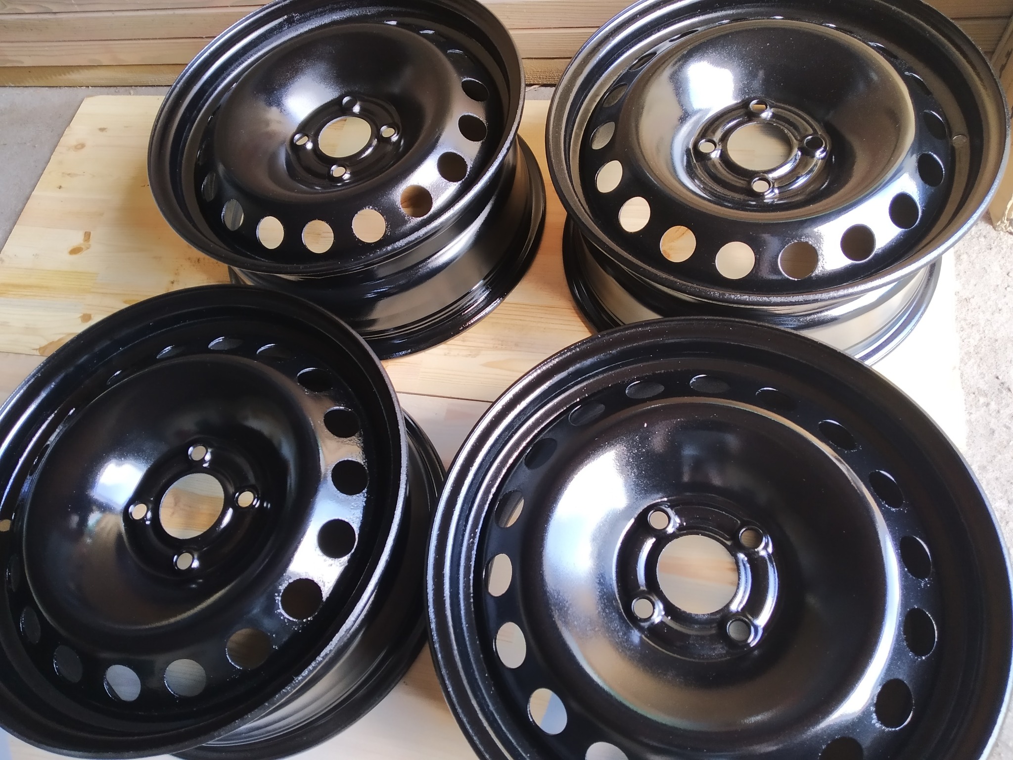 Cztery czarne, stalowe felgi samochodowe ułożone na drewnianej powierzchni, prezentujące świeżą, błyszczącą powłokę.
