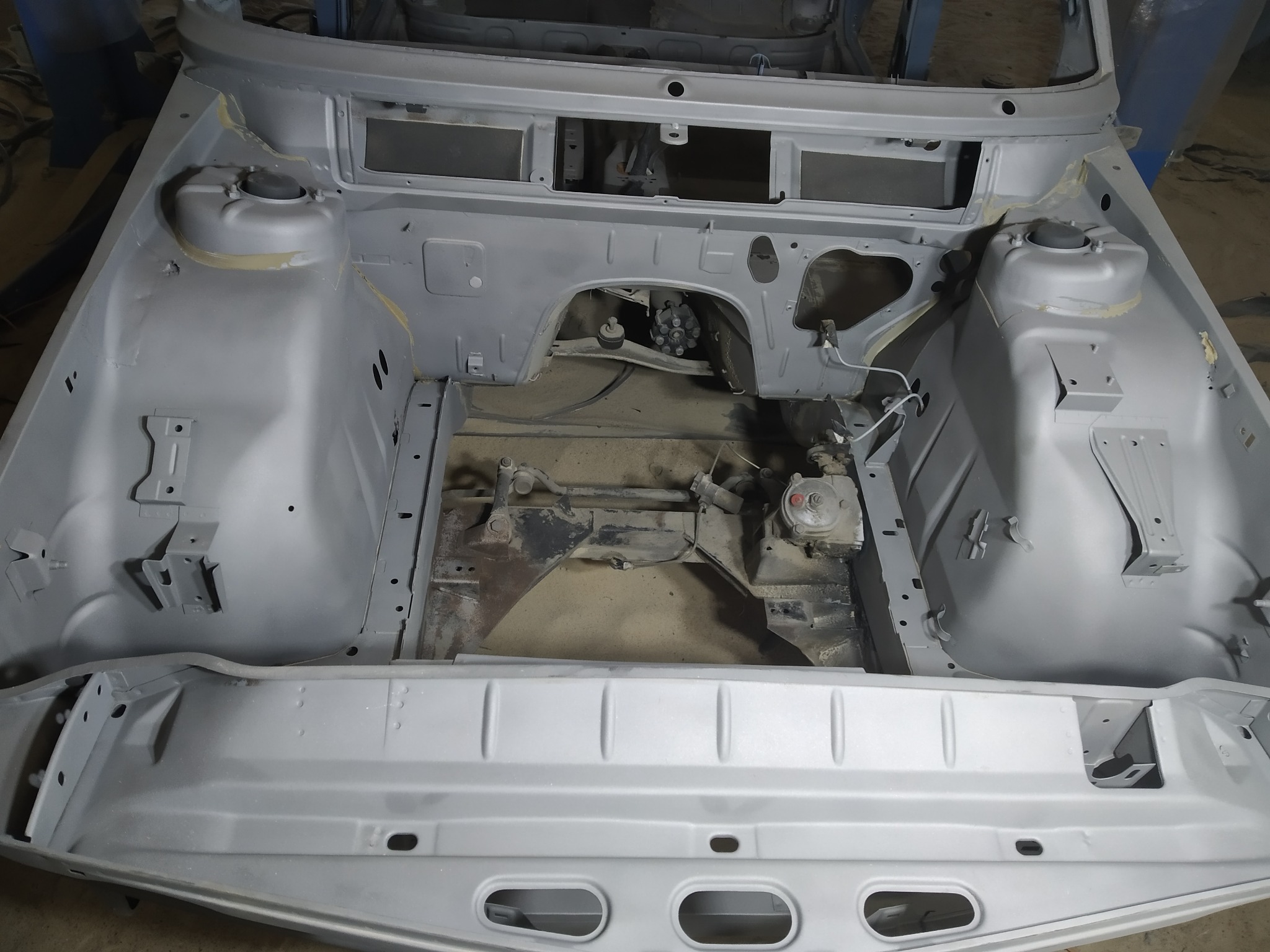 Wnętrze karoserii samochodu po oczyszczeniu i nałożeniu podkładu, przygotowane do dalszych prac lakierniczych. Widoczne elementy zawieszenia i mocowania.