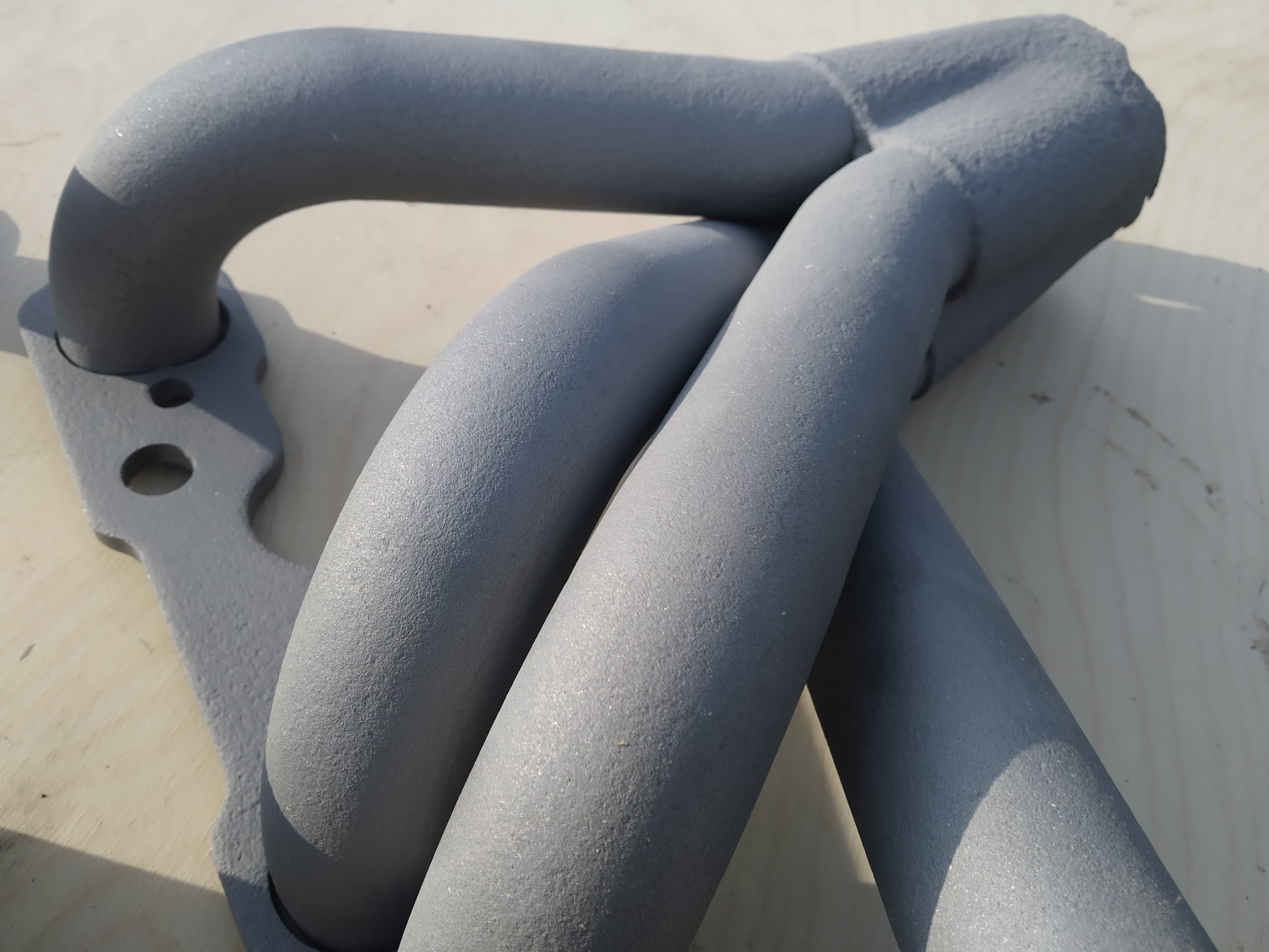 Kolektor wydechowy pomalowany szarą farbą proszkową, widoczne detale struktury farby.