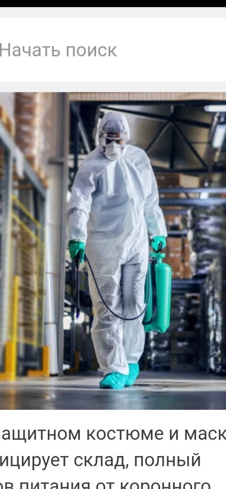 Pracownik w kombinezonie ochronnym, masce i okularach ochronnych, z zielonym opryskiwaczem, dezynfekuje magazyn z metalowymi regałami wypełnionymi kartonami.