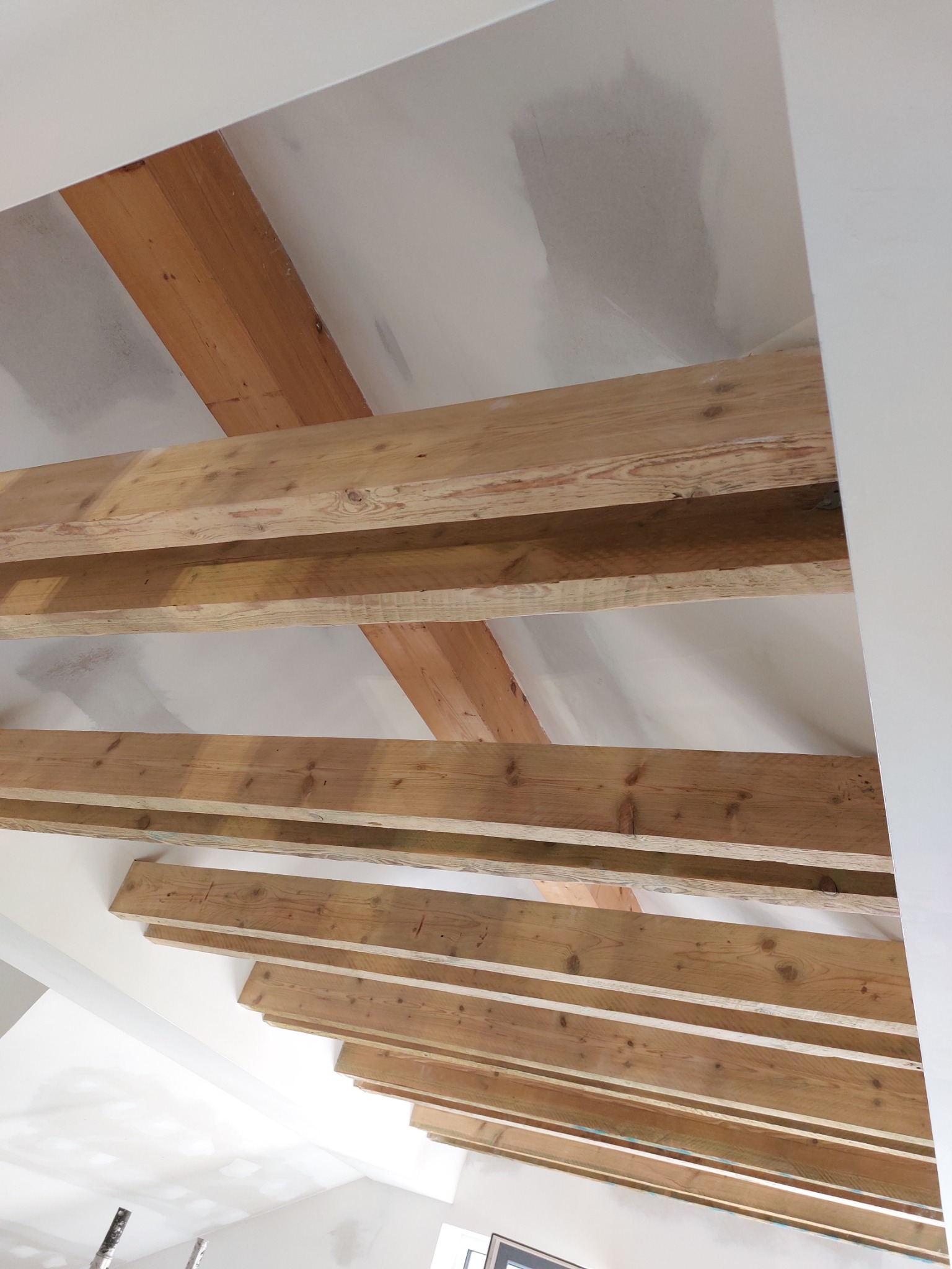 Drewniane belki stropowe poddasza z widocznymi śladami szpachlowania na płycie karton gips, przygotowane do dalszych prac wykończeniowych.