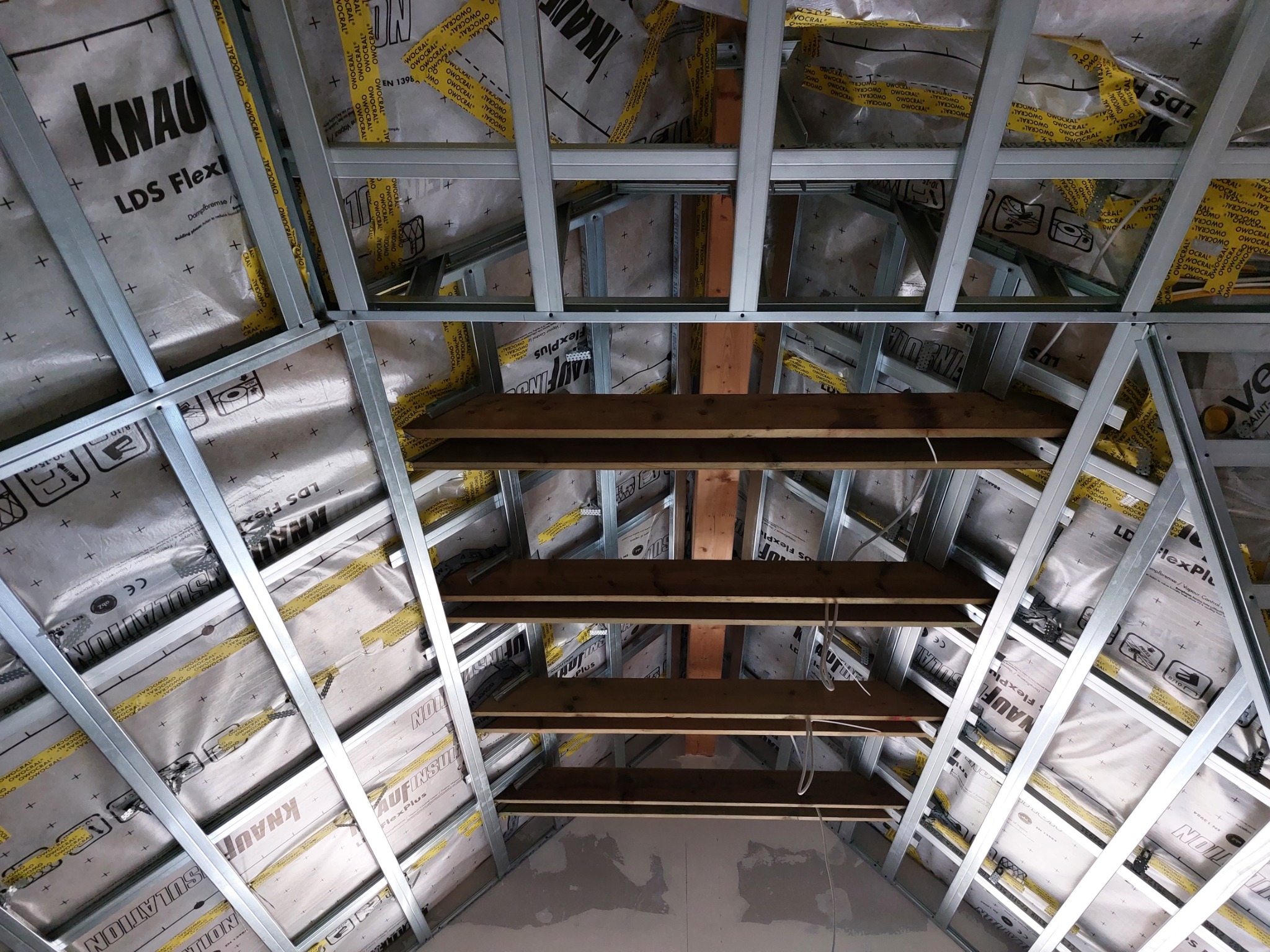 Konstrukcja poddasza z metalowych profili, izolacją Knauf i drewnianymi belkami, widok od dołu w trakcie prac.