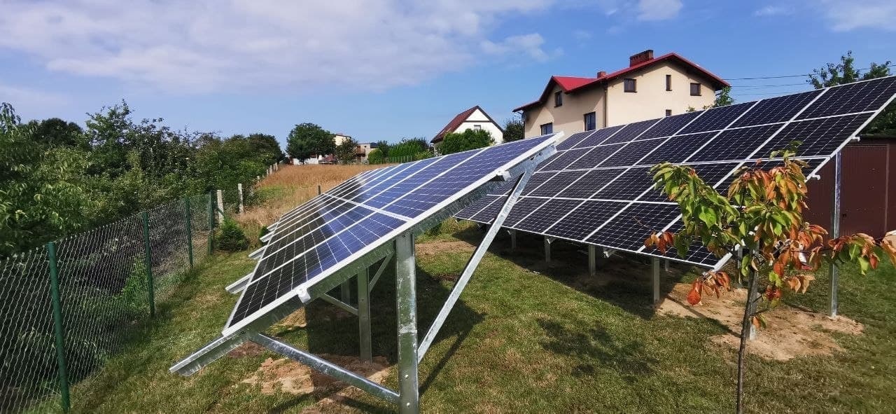 Instalacja paneli słonecznych na stelażach na trawiastym terenie w Krakowie, widok na domy w tle.