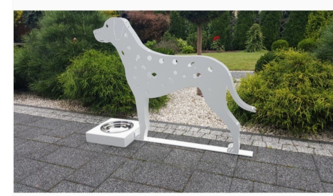 Metalowa, dekoracyjna sylwetka dalmatyńczyka z miską na karmę na tle ogrodu z kostki brukowej.