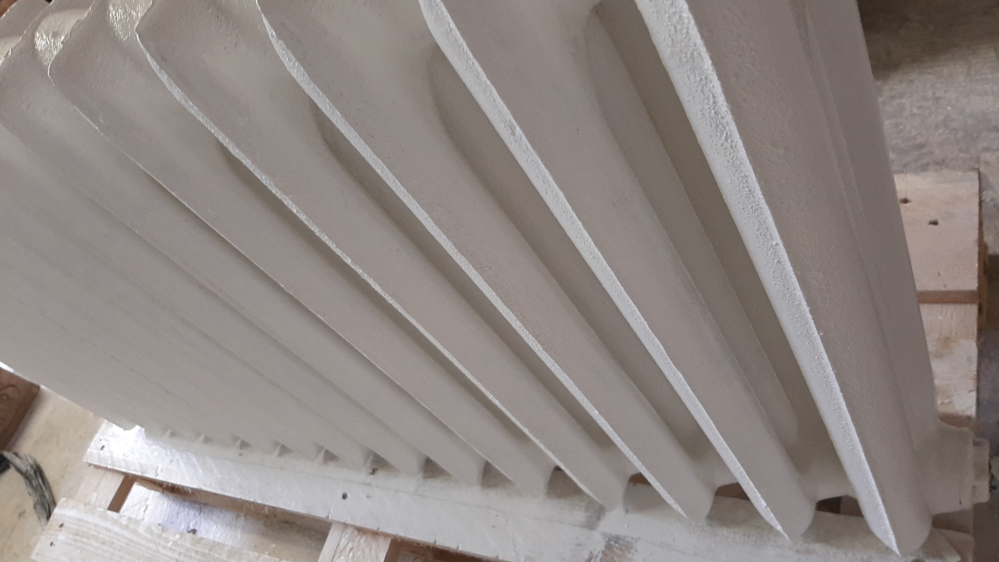 Biały, żeliwny grzejnik po renowacji, leżący na drewnianej palecie, widoczne detale chropowatej powierzchni.