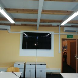 Instal-Went Baranowski Przemysław Psota Jarosław Spółka Cywilna - Sala biurowa z dwoma klimatyzatorami ściennymi, ekranem telewizora, trzema szafkami i widocznym wyjściem ewakuacyjnym.