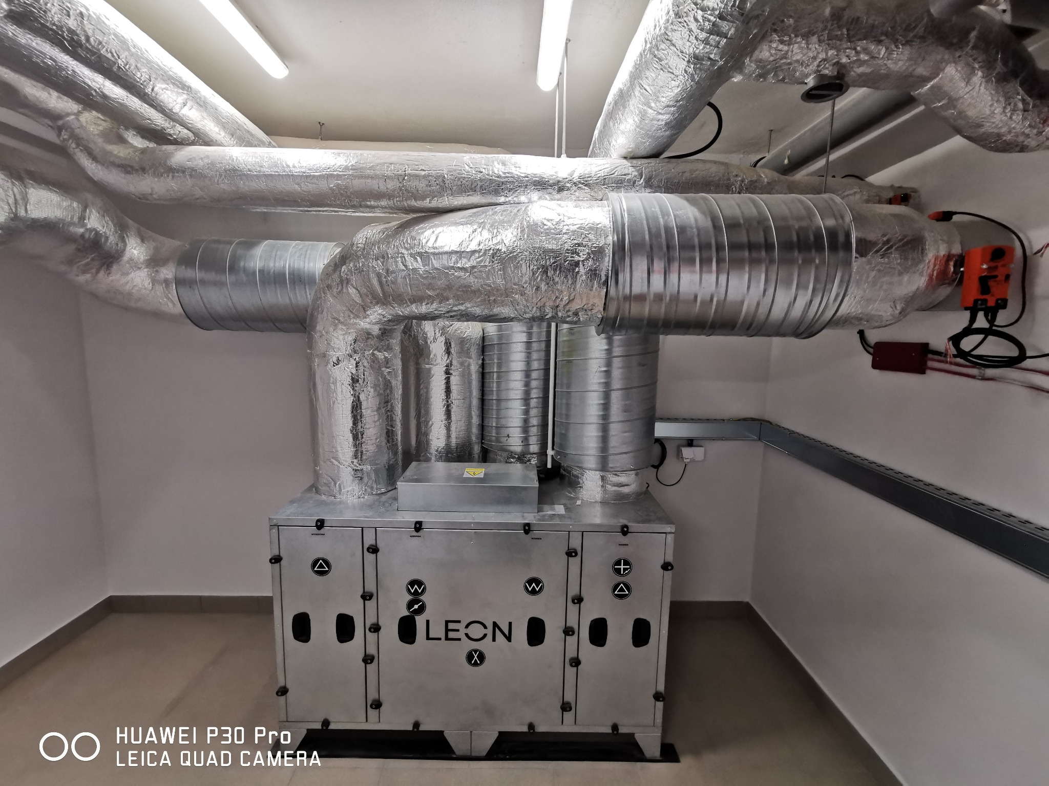Centrala wentylacyjna LEON X z izolowanymi przewodami w pomieszczeniu technicznym, widoczna instalacja elektryczna.
