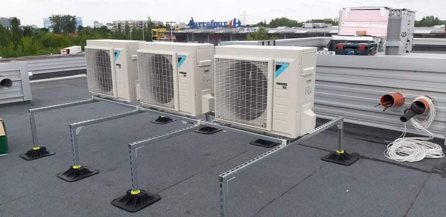 Trzy jednostki zewnętrzne klimatyzacji Daikin zamontowane na metalowej konstrukcji na dachu budynku, widoczne przewody i narzędzia instalacyjne, w tle budynek z logo Carrefour.