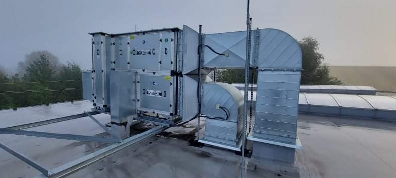 System wentylacyjny z metalowymi kanałami i centralą, zamontowany na dachu budynku komercyjnego w pochmurny dzień.