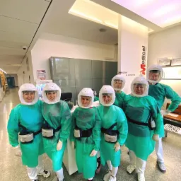 Zespół medyczny w kombinezonach ochronnych i przezroczystych hełmach z filtrami, pozujący w jasnym wnętrzu kliniki z logo 'Medical dr Irena Przybylska' w tle.