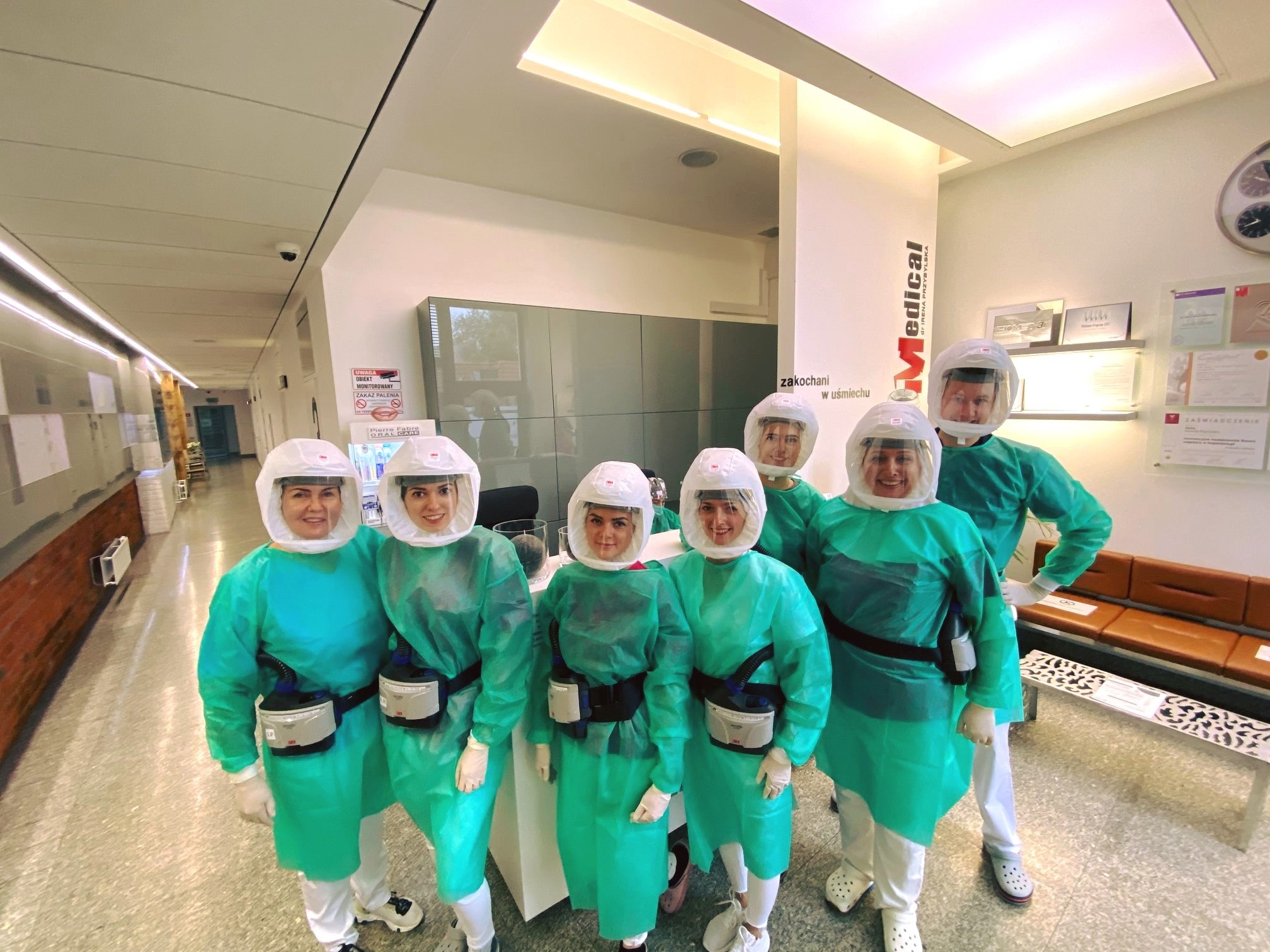 Zespół medyczny w kombinezonach ochronnych i przezroczystych hełmach z filtrami, pozujący w jasnym wnętrzu kliniki z logo 'Medical dr Irena Przybylska' w tle.