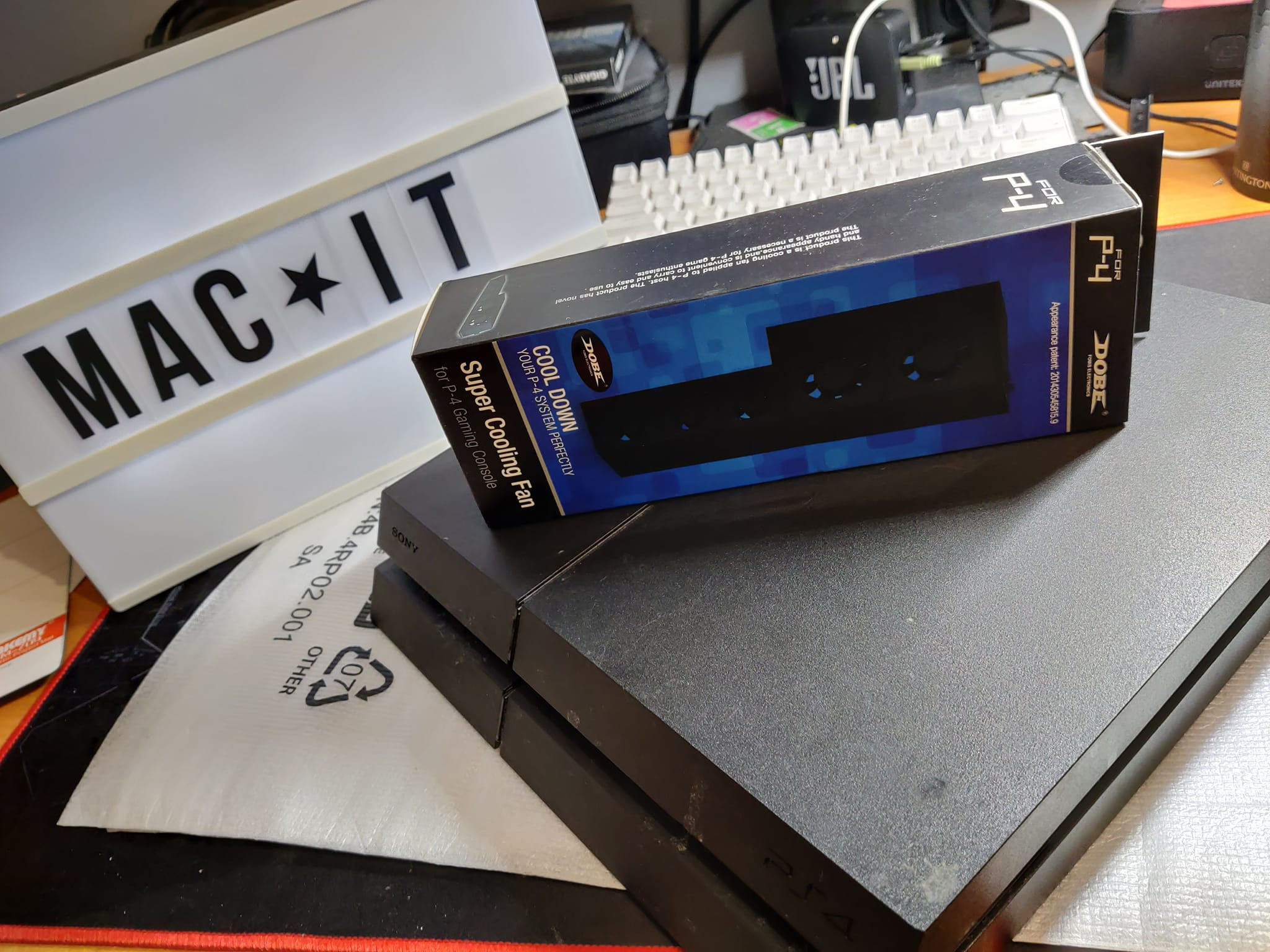 Czarna konsola PlayStation 4 z pudełkiem chłodzenia DOBE na górze, obok podświetlany napis MAC IT oraz klawiatura w tle.